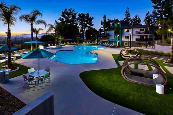 Hotel-style amenity with curved concrete pool deck, synthetic turf, and palm trees overlooking a Southern California sunset in the valley