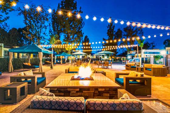 Outdoor hotel-style amenity at a multi-family residence featuring sofas around a firepit, string lights, and cabanas