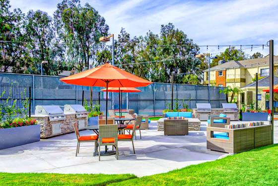 Grill deck with large raised planters, four grills, string accent lights, and a tennis court with a Southern California blue sky